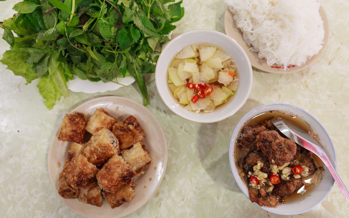 Bún chả. Smoky grilled pork — both caramelised slices and juicy patties — is served in a bowl of warm, lightly sweetened fish sauce with pickled green papaya and carrot.