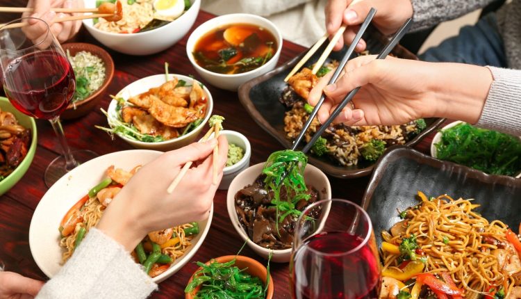 Guests sharing an authentic Asian communal dining feast with noodles, dim sum, and red wine, showcasing boutique culinary travel experiences.