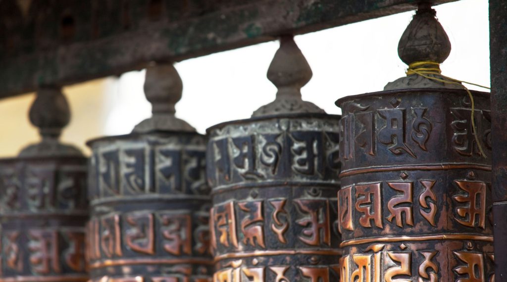 Close-up of embossed metal prayer wheels inscribed with sacred Tibetan mantras hanging in a row