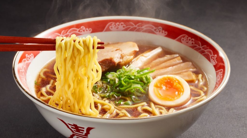 Steaming bowl of authentic Japanese ramen with sliced pork, bamboo shoots, and soft-boiled egg, reflecting regional culinary experiences in Asia.
