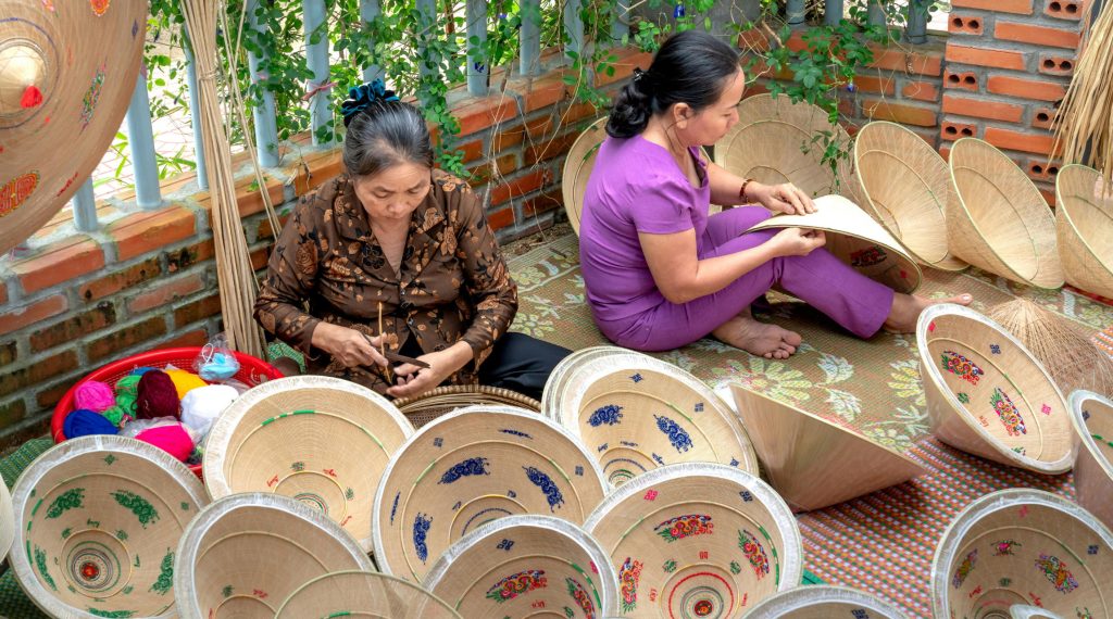 Vietnamese artisans crafting traditional palm-leaf conical hats (Nón Lá) decorated with intricate interior embroidery.