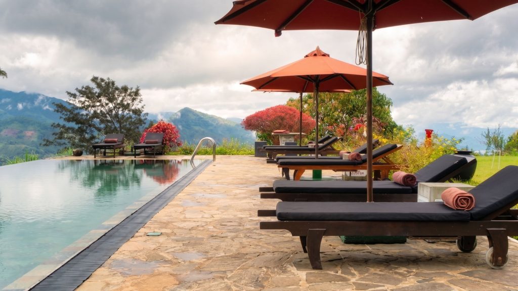 Infinity pool and sun loungers overlooking misty mountain peaks at a luxury highland tea estate resort