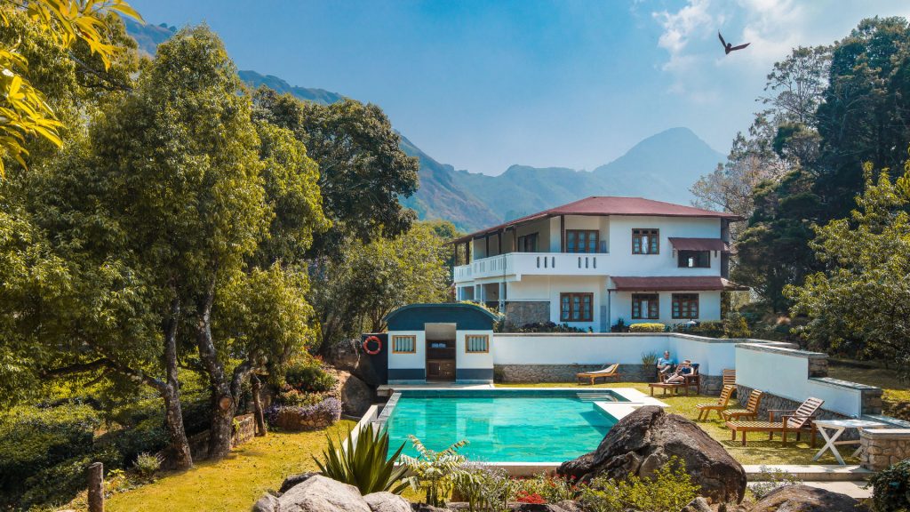 Colonial-style estate and outdoor swimming pool surrounded by lush green hills and tea plantations in Munnar