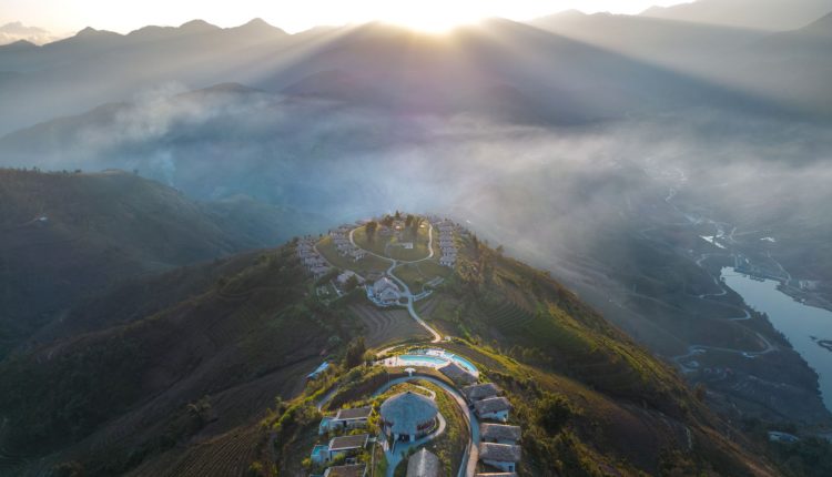 Aerial sunrise view of an eco-lodge perched on a misty mountain peak above terraced valleys