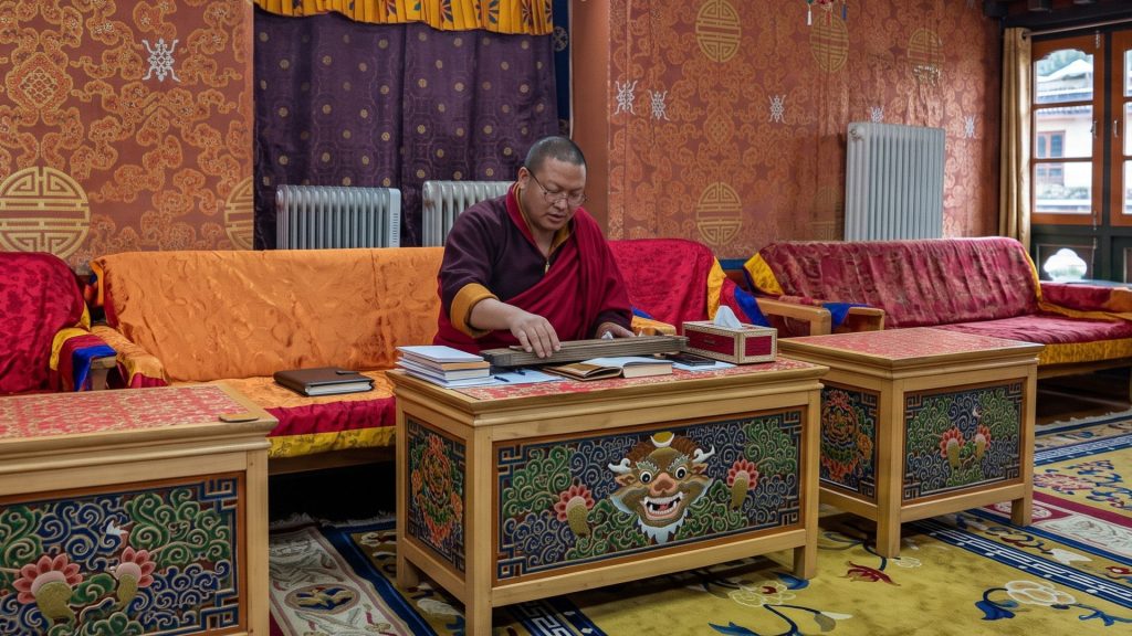Buddhist monk studying sacred pecha scriptures in an ornate, traditionally painted temple hall
